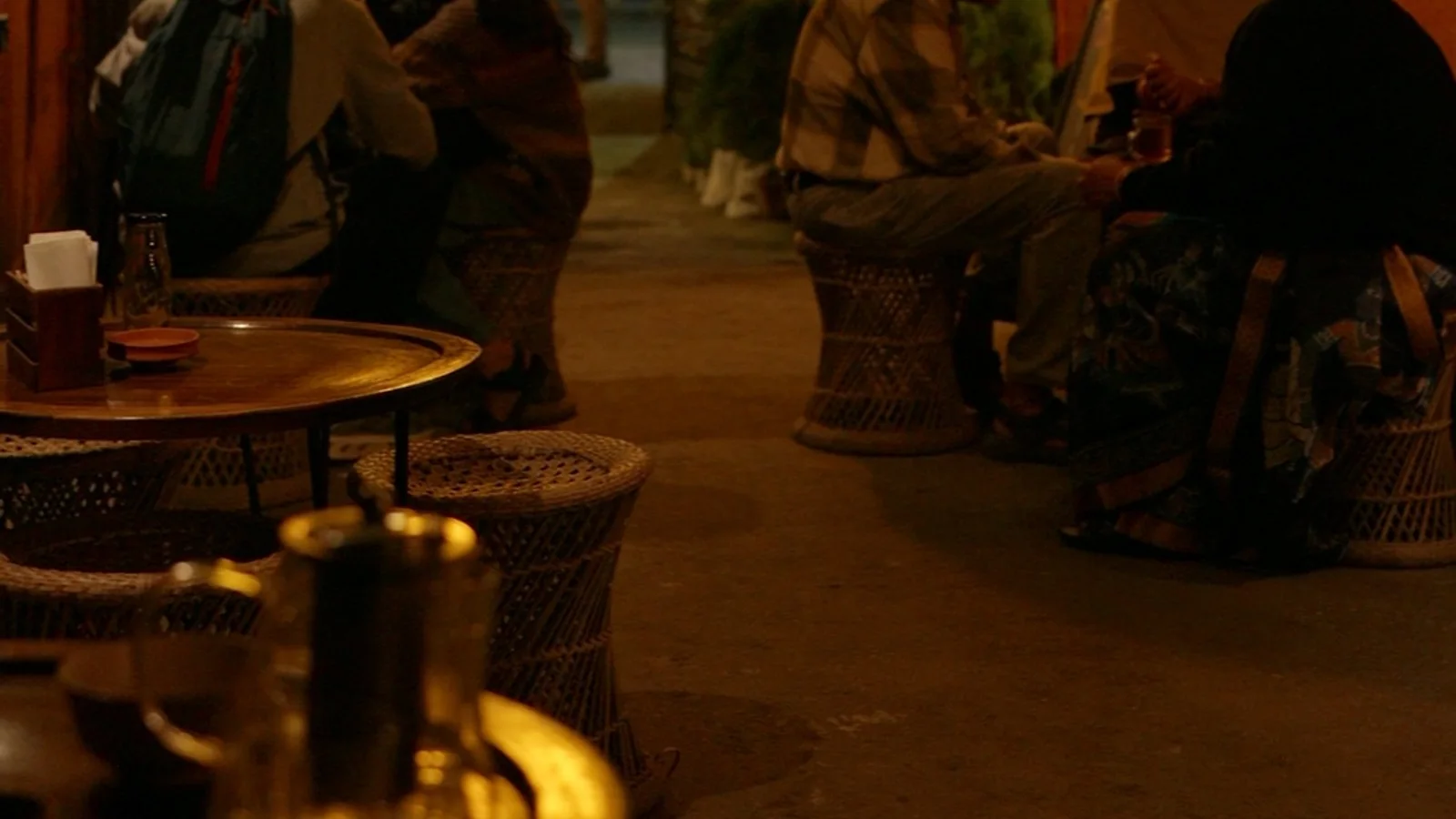 An evening gathering inside Art-Teas-Tree — warm pendant lights, orange walls, visitors in quiet conversation